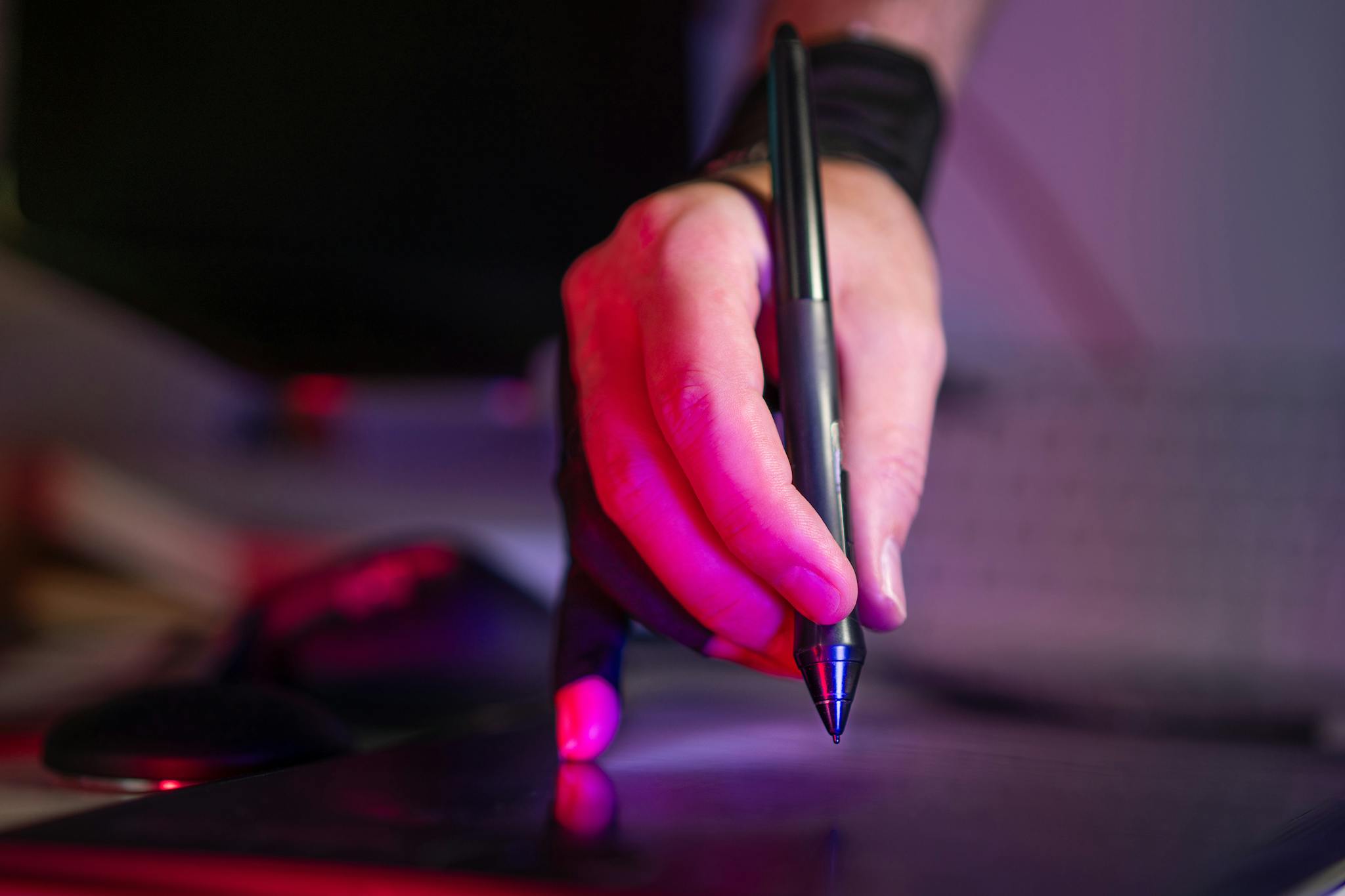 A digital artist's hand working on a graphics tablet with a stylus, in a creative studio setting.