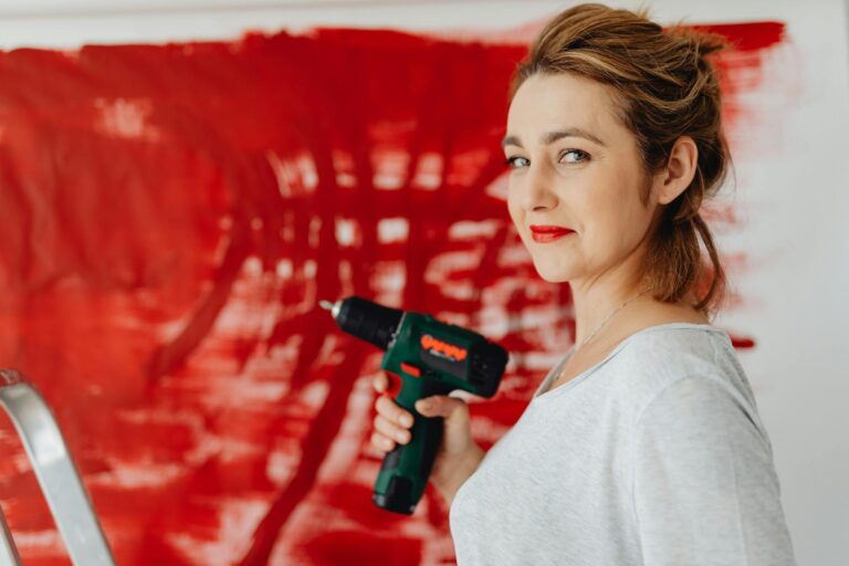 Woman using drill in front of red painted wall, showcasing empowerment.